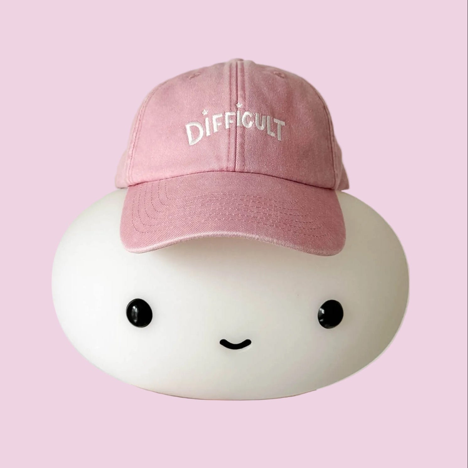 Pink cap with 'DIFFICULT' text on a white background