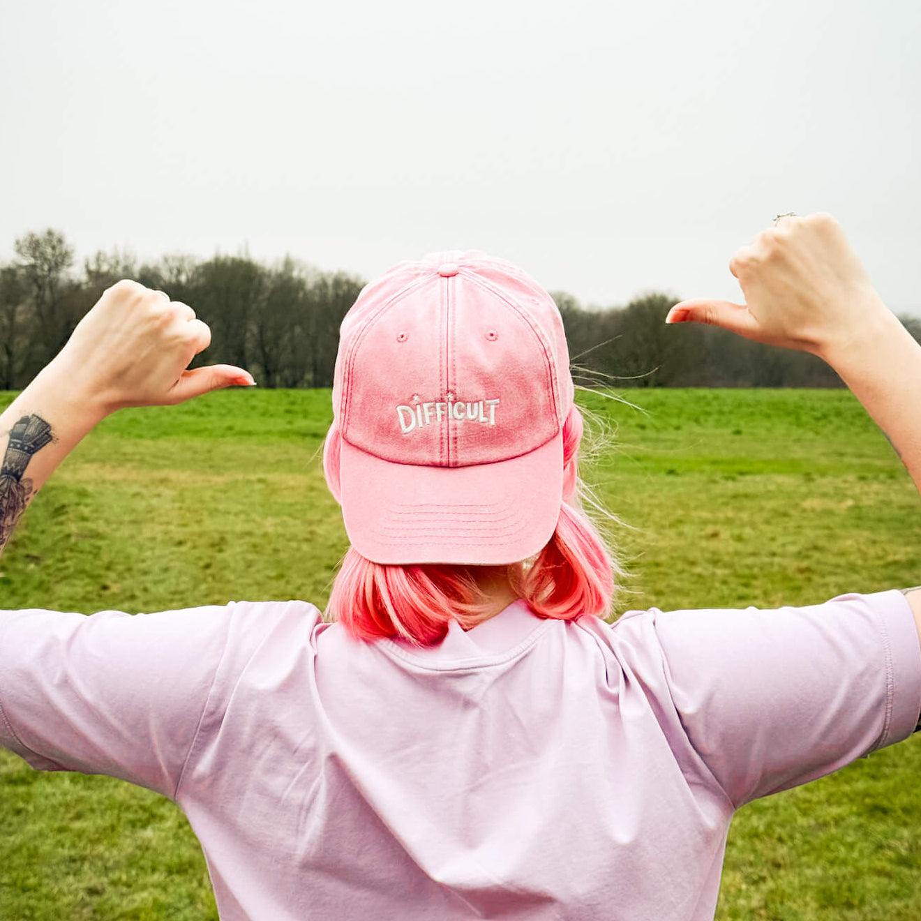 Person wearing a pink cap and shirt with arms outstretched in a field